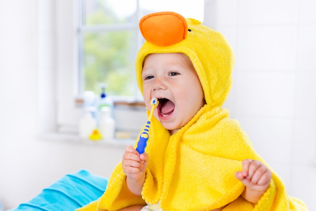 Toddler in a towel brushing their teeth.